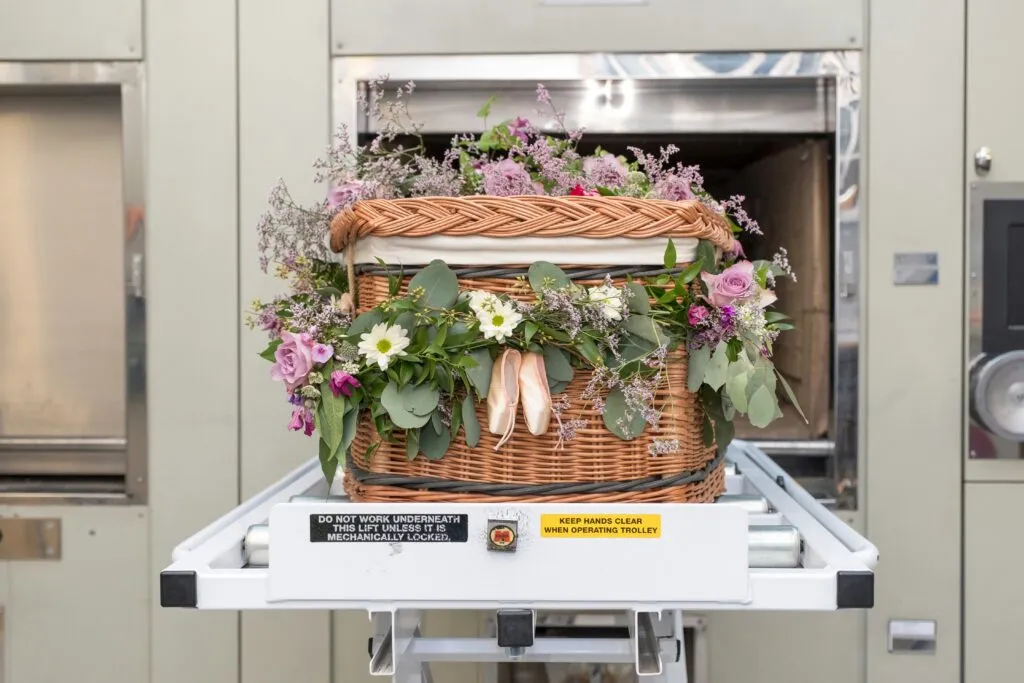 Cercueil tressé en osier orné de fleurs champêtres et de chaussons de danse