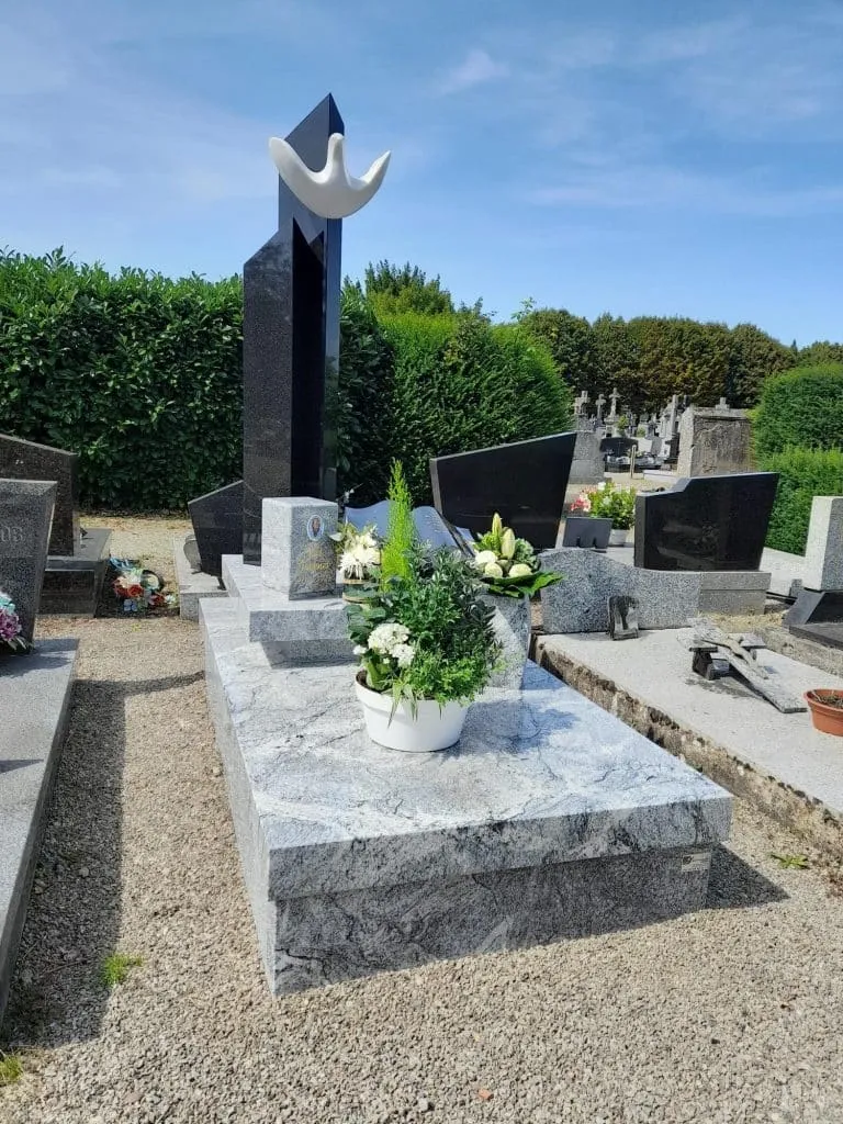 Monument funéraire en granit gris poli orné de fleurs et plaques commémoratives dans un cimetière